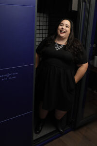 Maria Pendolino, Voiceover Artist for News Talk Radio Imaging, in a black dress, standing on her recording booth 